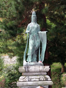 観世音菩薩（乙女が即身成仏して観音さんに化身した銅像、右手にハサミ、左手に長い布をもつ）