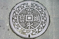 琴弾公園の砂上の芸術銭形「寛永通宝」と市の木「マツ」が描かれた観音寺市のマンホールです。