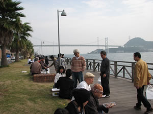 桟橋で関門橋を見ながら海の幸を食べる観光客。